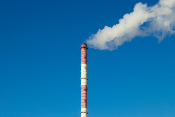 High red and white striped tube lets out white smoke into clear blue sky. Small cloud above pipe on...