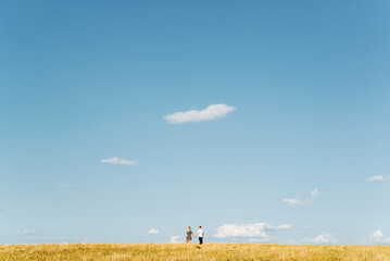 Couple walking in picturesque field holding hands, standing far on horizon against blue sky and looking at each other. Romantic trip, love and relationships