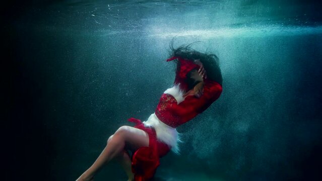graceful sexy lady in red is swimming underwater, fantastic winter fairytale