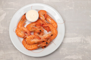 Boiled fresh shrimps with sauce in small bowl on white plate on ceramic