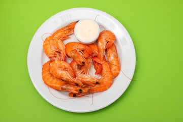 Boiled fresh shrimps with sauce in small bowl on white plate on green