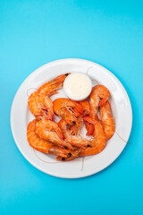 Boiled fresh shrimps with sauce in small bowl on white plate on blue
