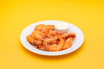 Boiled fresh shrimps with sauce in small bowl on white plate on yellow
