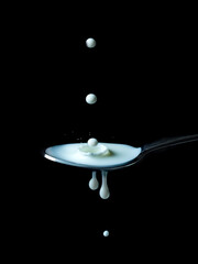 Spoon with milk on a black background and a drop of milk.