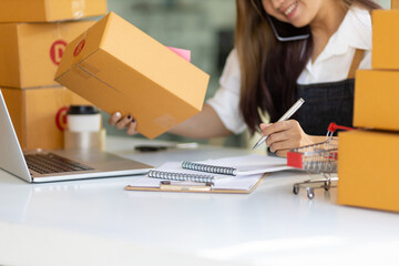 A woman doing an e-commerce business is talking on the phone with a customer and writing a note.