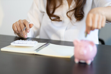 A woman puts coins in a piggy bank and writing a note in the financial book. Money saving concept.