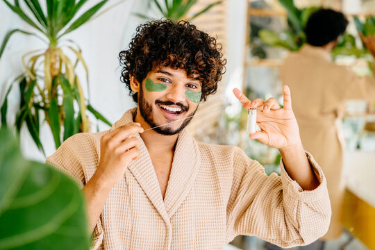 Happy asian hispanic man in bathrobe with wide healthy smile using dental floss, cleaning teeth, looking at camera, dental care, oral hygiene concept in bathroom home interior.