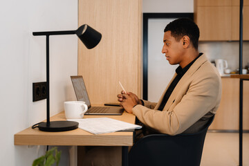 Black man wearing jacket working on laptop while sitting at desk