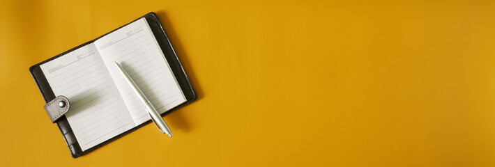 An open notebook or diary with a leather cover and a silver fountain pen lie on a yellow surface....