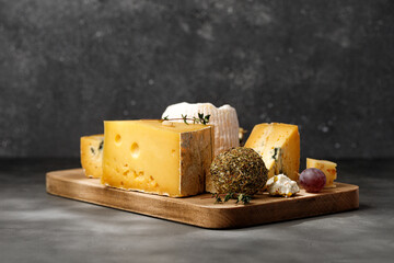 Assortment of different cheese types on wooden board on dark background.