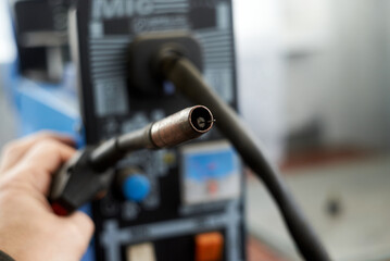 A human hand holds a burner that feeds wire for welding parts.