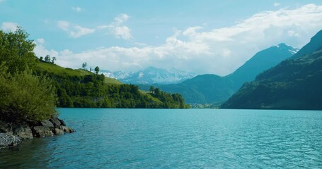 Picturesque view of lake in Brienz Switzerland at noon as water ripples calming move towards shore with cloudy mountains in the distance in Europe, wide view
