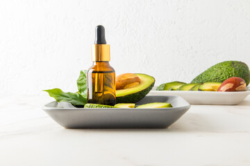 cosmetic bottle with a dropper pipette made of brown glass with a therapeutic serum on a gray ceramic tray with avocado fruit.