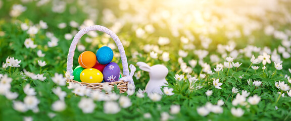 Panoramic view of the spring field with rabbit toy and bascket with colourful eggs on it.