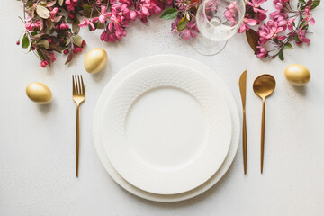 Easter festive dinner with golden eggs, festive tableware and flowers on white background. Top view. Festive tablescapes.