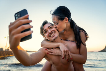 lifestyle photoshoot of young helthy beautiful caucasian couple, active boy and girl, dating at the beach - Man and woman lovers having fun in holidays taking selfies near the ocean in a sunny day