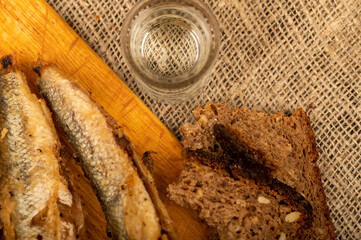 A small fried fish on a wooden board, pieces of bread and a glass of vodka, close-up, selective focus.