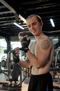 Portrait of smiling young man putting on wrist support gloves before lifting weights in gym