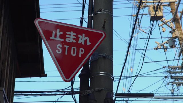 Red triangular stop warning traffic road sign with white letters kanji standing at the local street junction in Japan. Translation of the word in Japanese means stop