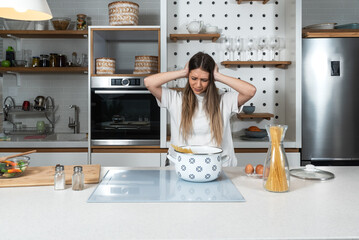 Young confused woman standing in her kitchen wandering wats wrong with brand new broken cooktop she bought when she cant cook food and heat the water to boiling temperature and all lamps work fine - obrazy, fototapety, plakaty