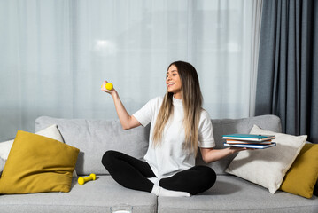 Young happy fitness college student woman sitting at home study reading books to educate herself...