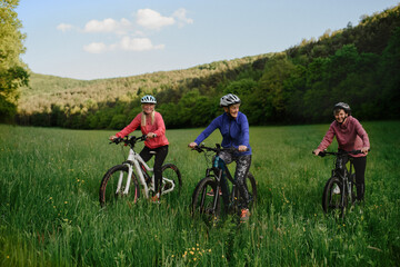 Happy active senior women friends cycling together outdoors in nature.