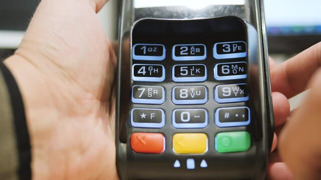Male hand dialing pin code on pin pad of pos terminal close-up