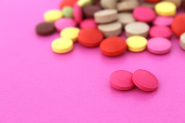 Two pink pills lie on a pink background and a bunch of different pills.