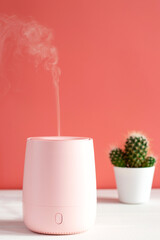 Humidifier or aroma lamp turned on the table against pink wall with home plant. The concept healthy lifestyle, and comfortable living conditions