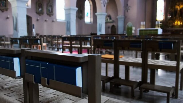 Empty catholic cathedral inside, wooden benches for prayers, ornament, interior. Wooden pews for church members. Inside an empty catholic church illuminated by sun rays. Small Chapel. Panning shot. 4K