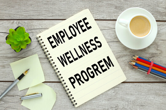 EMPLOYEE WELLNESS PROGREM Open laptop with office supplies on a wooden table. colored pencils