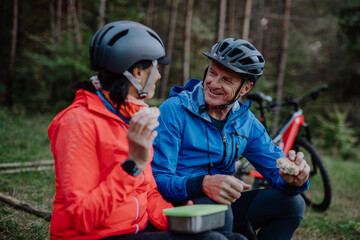 Happy senior couple bikers with eating snack outdoors in forest in autumn day.