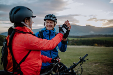 Senior couple bikers high fiving outdoors in nature in autumn day.