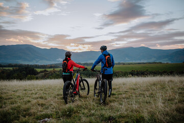 Fototapeta premium Rear view of senior couple bikers walking and pushing e-bikes outdoors in forest in autumn day.