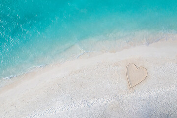 Perfect drawing of heart shape in soft sand beautiful seascape background. Romantic Valentine's day or love beach scene, top aerial view. Romance, honeymoon in vacation, summer travel. Idyllic nature
