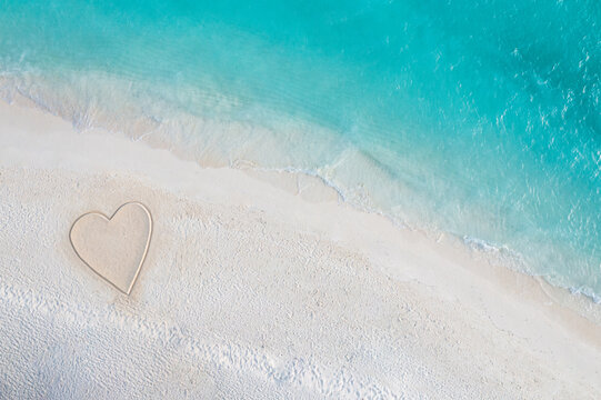 Perfect drawing of heart shape in soft sand beautiful seascape background. Romantic Valentine's day or love beach scene, top aerial view. Romance, honeymoon in vacation, summer travel. Idyllic nature