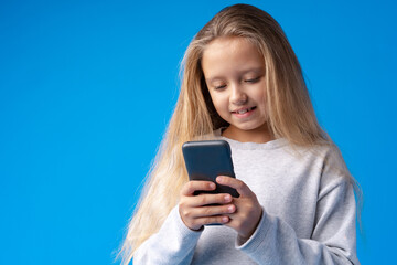 Fototapeta premium Little girl using mobile phone.against blue background