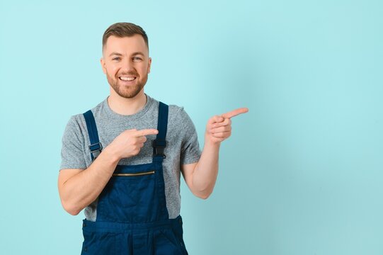Young electrician man or Craftsmen over isolated blue wall pointing to the side to present a product