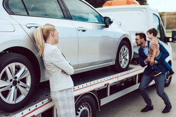 An agitated family with a small child wait for a tow truck to take away their broken car.