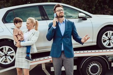 An agitated family with a small child wait for a tow truck to take away their broken car.