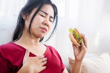 Asian woman having heartburn, acid reflux after eating burger, eating junk food concept