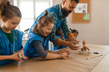 Group of little kids with teacher working with pottery clay during creative art and craft class at school.