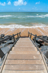 Beachfront landscape of a wooden stair leading down to the sea, beautiful blue sky day. Boa Viagem beach in Recife, PE, Brazil.