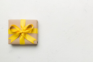 Holiday gift box wrapped in craft paper with colored bow on table background. Top view, flat lay, copy space