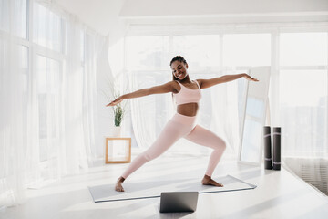 Fototapeta premium Joyful fit young black woman practicing yoga at home, standing in warrior pose, copy space