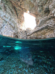 Underwater split photo of beautiful paradise pebble rocky bay of Kaladi with turquoise crystal clear sea and small caves, Kythira island, Ionian, Greece