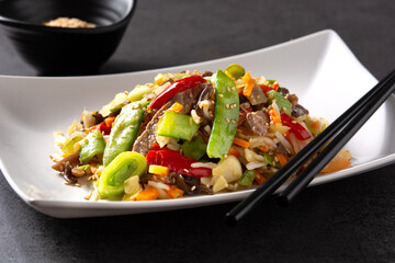 Beef, vegetables and sesame seeds in white plate on black background	