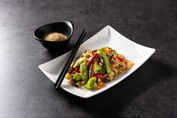 Beef, vegetables and sesame seeds in white plate on black background	