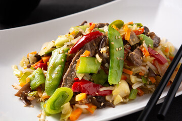 Beef, vegetables and sesame seeds in white plate on black background	