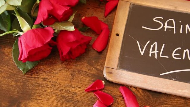 inscription saint valentin en Fran&ccedil;ais sur une ardoise avec des roses et des p&eacute;tale sur un fond en bois 